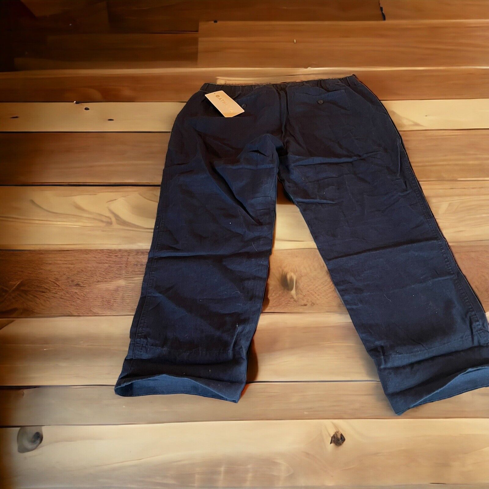 Dark navy Athleta linen ankle pants laid flat on wooden floor with tag attached