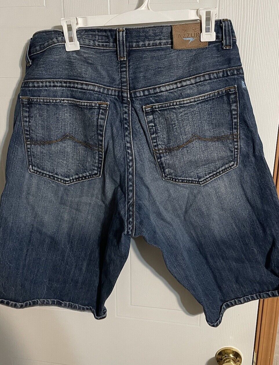 Back view of blue denim Azzure jorts men hanging on white hanger showing back pockets and belt loops