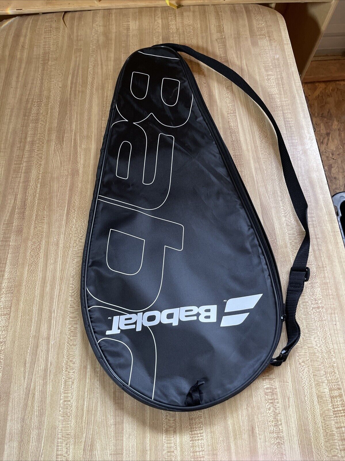 Black Babolat racquet cover with strap featuring white Babolat logo on wooden surface