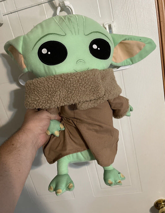 Baby Yoda plush toy with large black eyes and brown coat held against white door