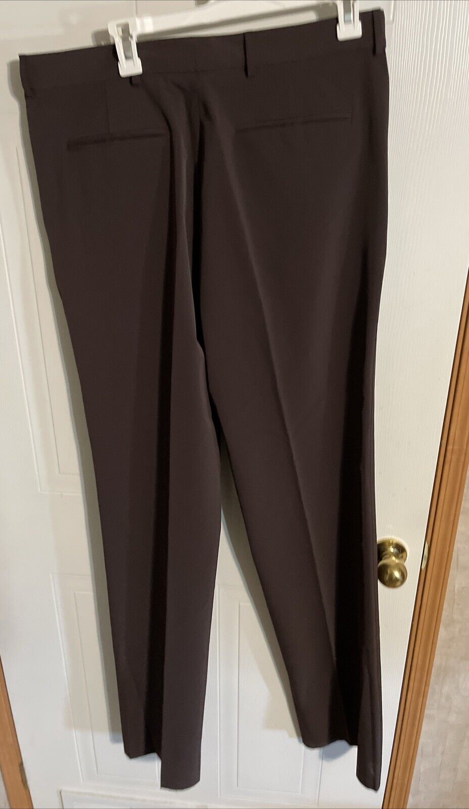 Brown Bally men’s dress pants hanging on white hanger against door background