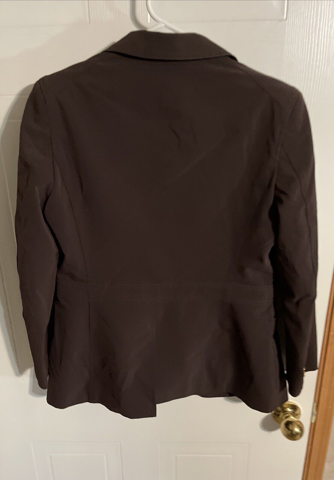 Back view of Bally women's black blazer hanging on a white hanger against a door background