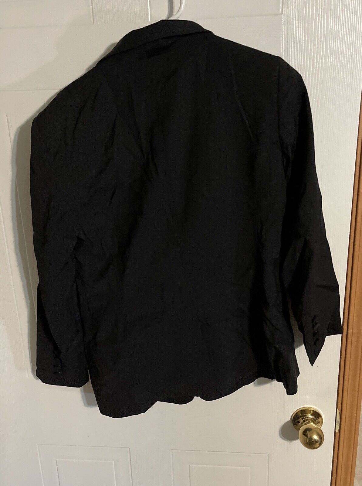 Bally women's black blazer hanging on white door showing back view with long sleeves