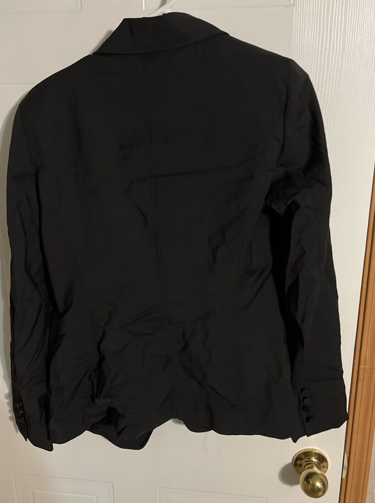 Back view of Bally women's black suit jacket hanging on white door with wrinkled fabric