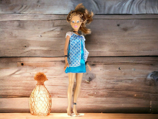 Barbie doll for sale dressed in blue polka dot outfit standing on wooden surface next to decorative bottle