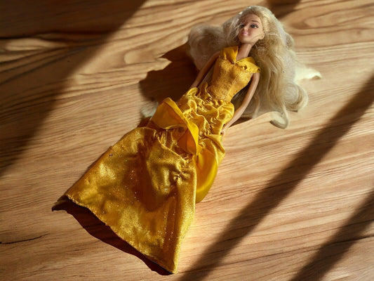 Barbie doll in yellow dress lying on wooden surface with detailed fabric and long blonde hair