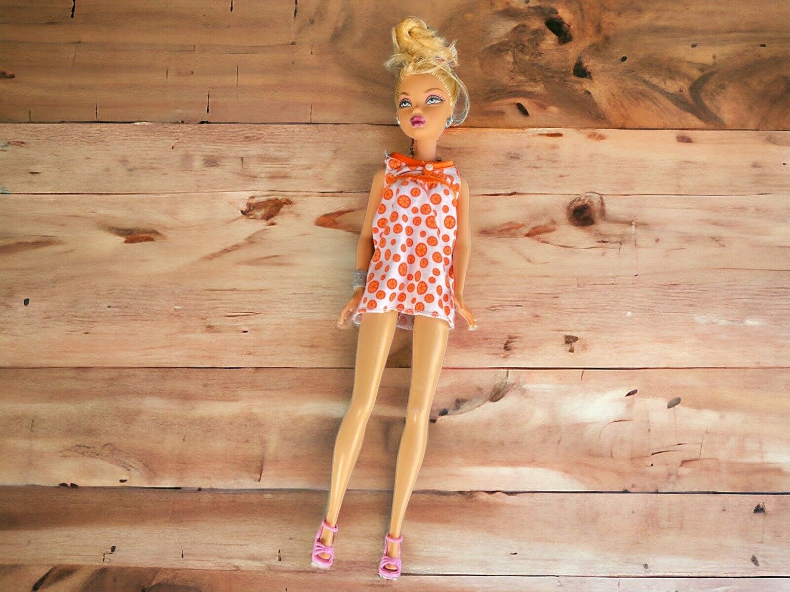Barbie doll with polka dot dress in white and orange wearing pink shoes on wooden background