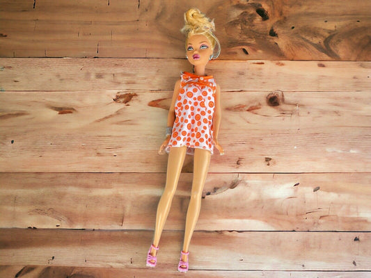 Barbie doll with polka dot dress in white and orange wearing pink shoes on wooden background