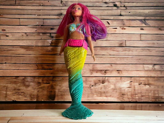 Barbie Dreamtopia mermaid doll with pink and purple hair and colorful green and yellow tail standing on wooden surface