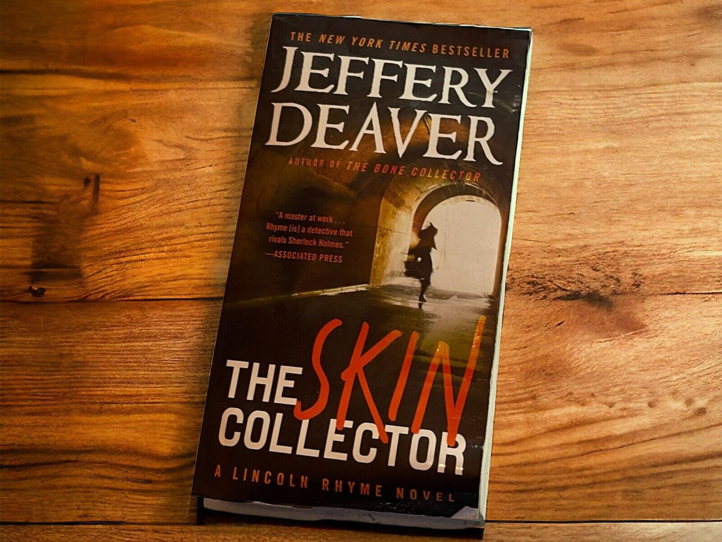 The Skin Collector book by Jeffery Deaver on a wooden surface featuring dark cover with silhouette figure
