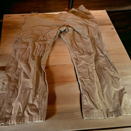 Beige mens tactical cargo pants laid out flat on wooden surface with multiple pockets