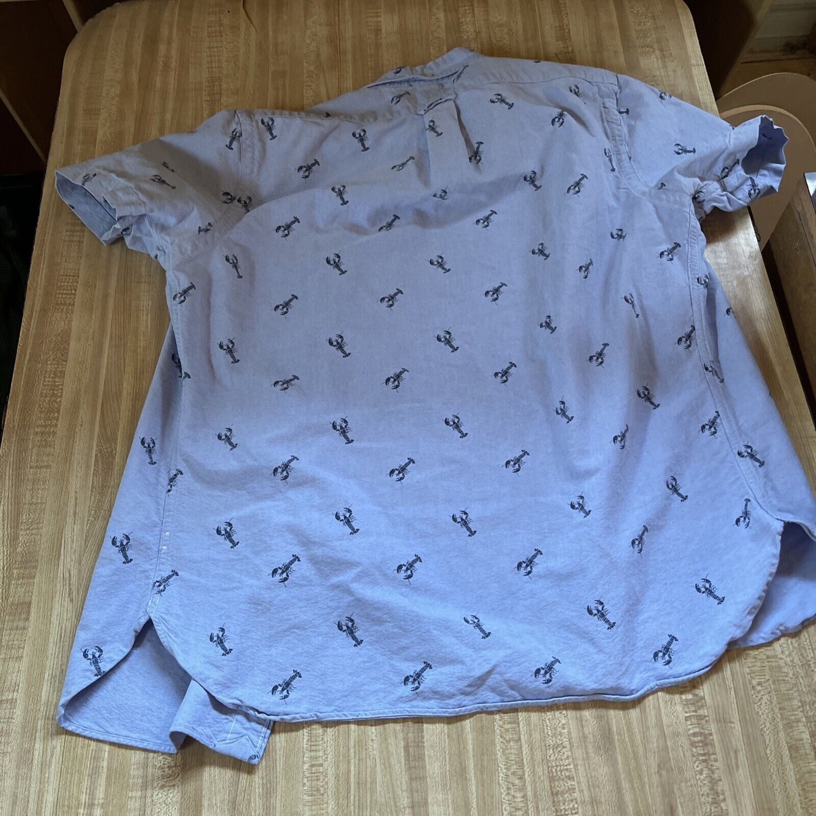 Light blue Ralph Lauren lobster print shirt with short sleeves laid flat on wooden surface
