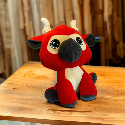 Red and black 2 foot tall plush toy with big eyes and white horns sitting on wooden table