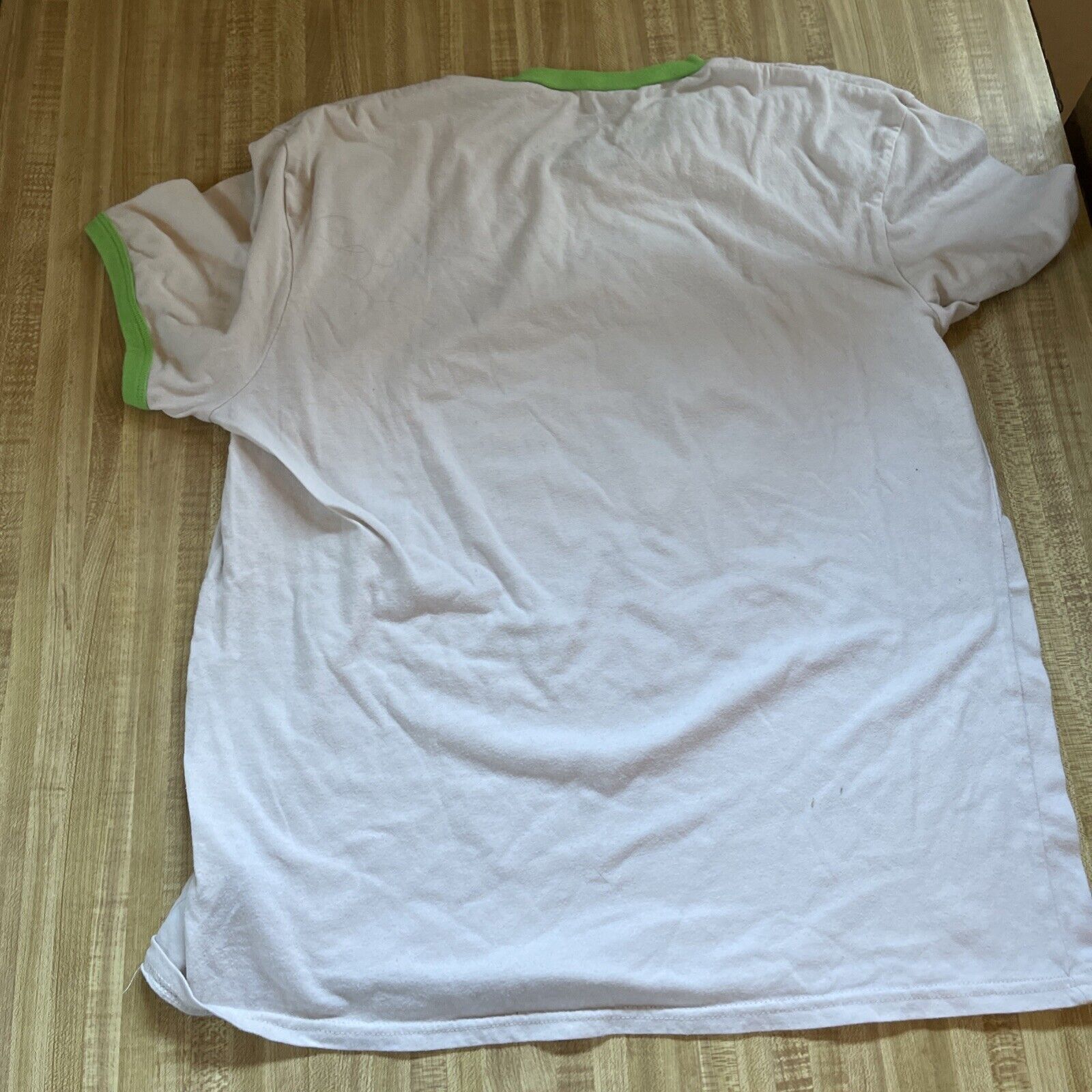 White Rick and Morty ringer t shirt with green collar and sleeve edges laid flat on wooden surface