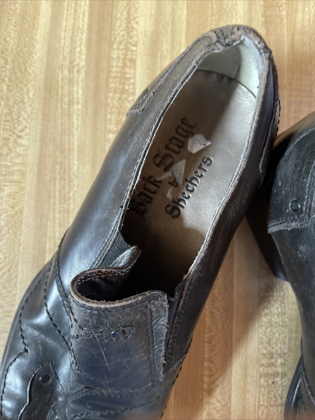 Close-up view of worn Back Stage by Skechers shoes in black leather on wooden floor