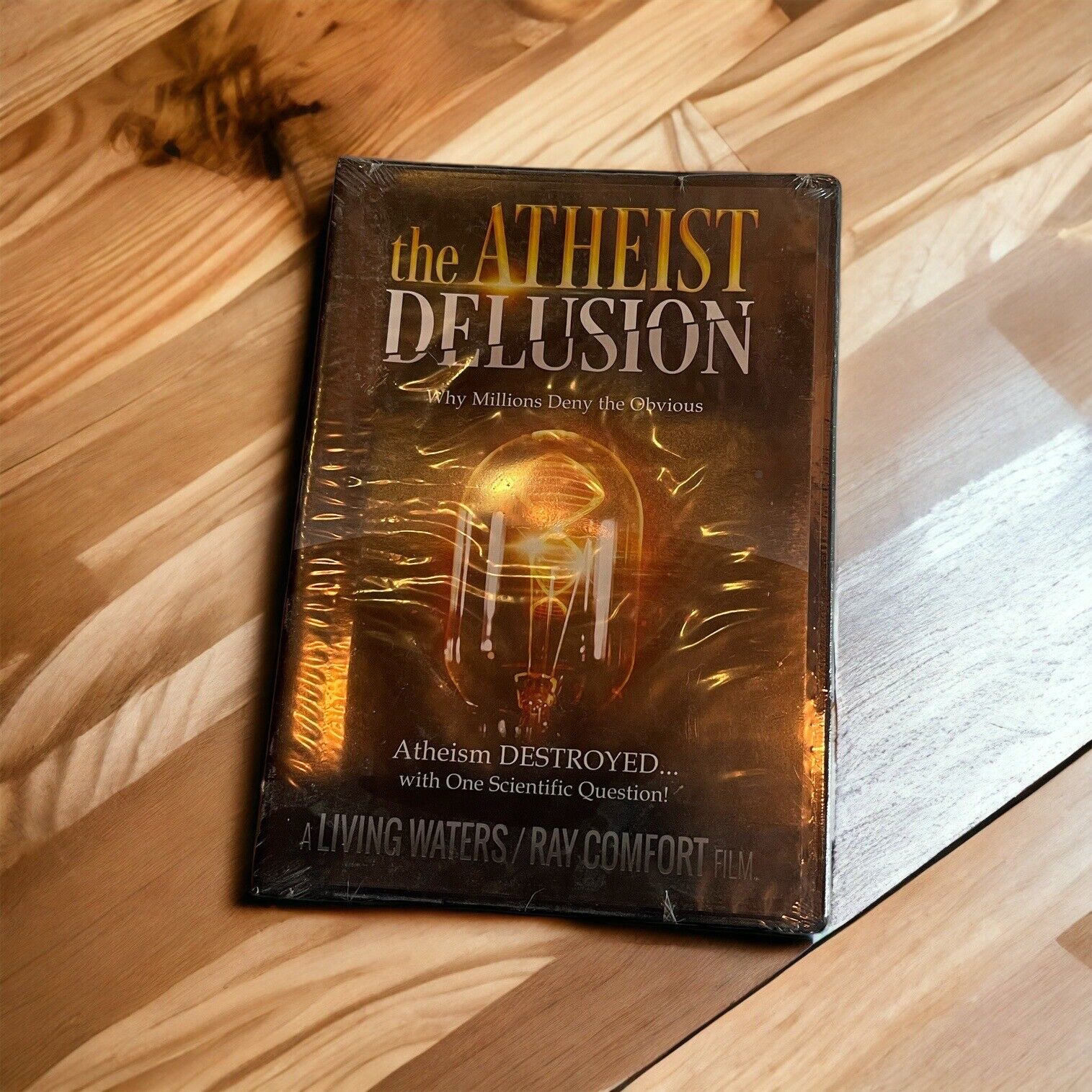 The Atheist Delusion DVD by 1118 Emporium with cover showing a glowing light bulb on wooden surface