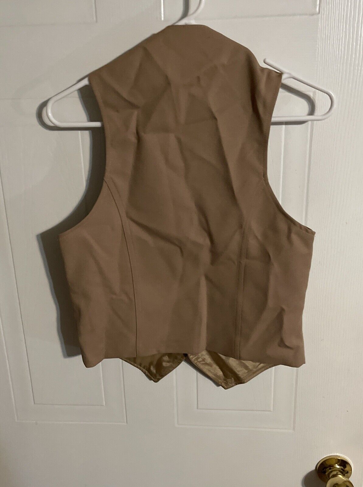 Back view of vintage Angel Flight vest in tan color hanging on white hanger
