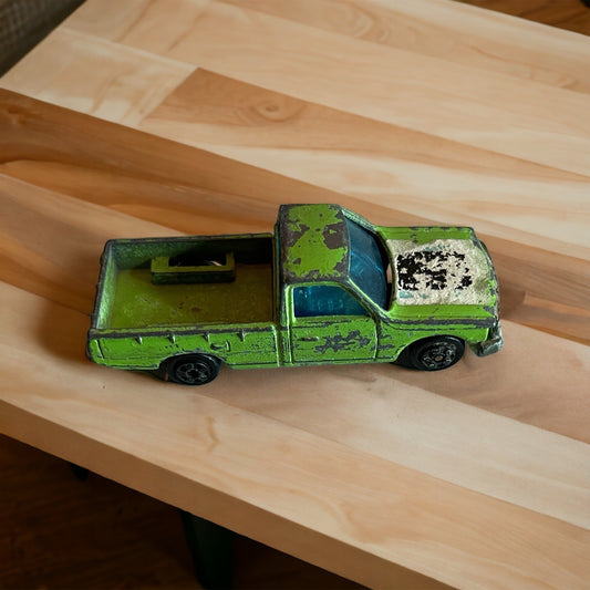 Vintage Zylmex Datsun pickup toy in green with worn paint on a wooden surface