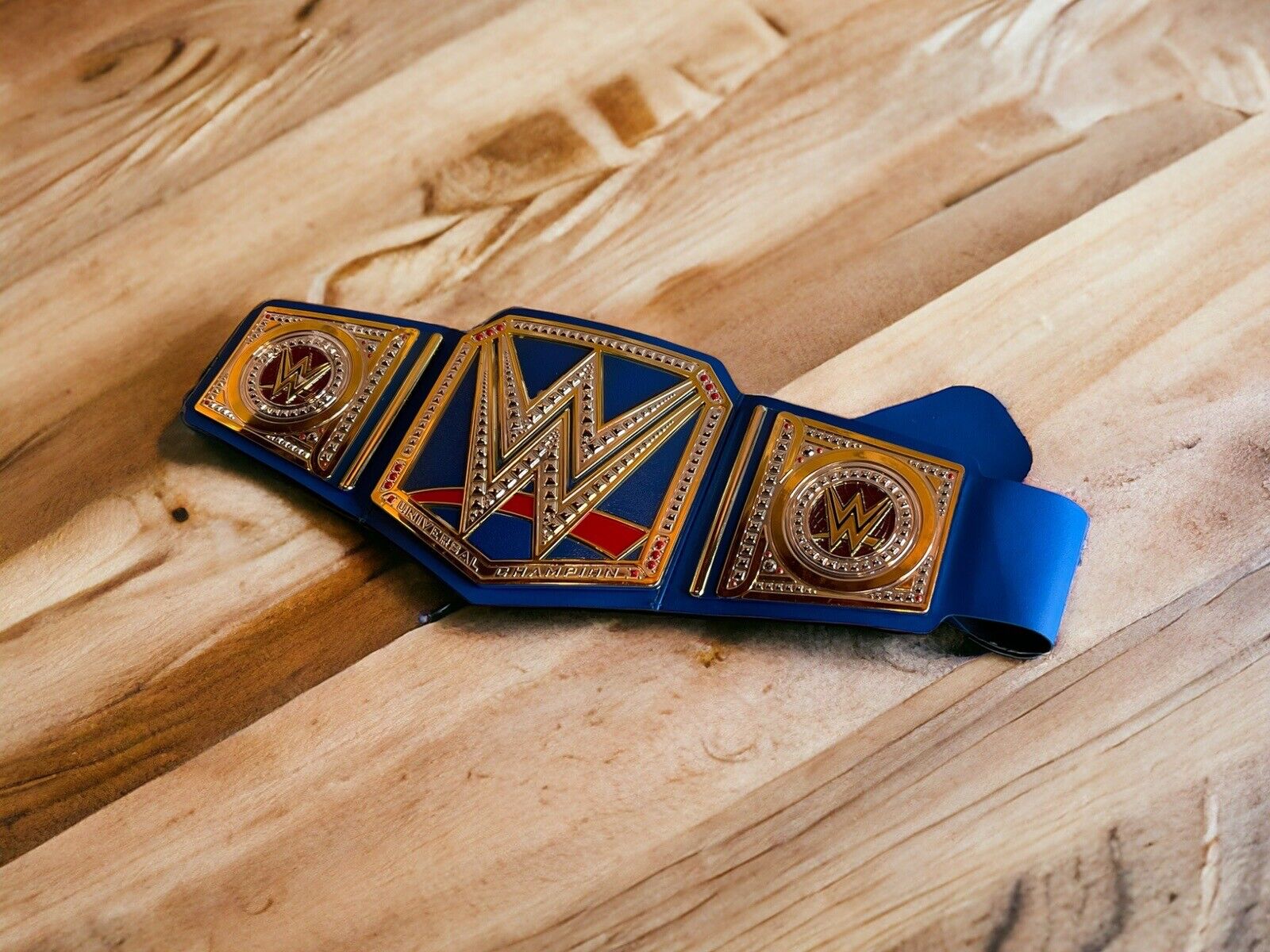 WWE Universal Champion replica belt with gold and blue design placed on wooden surface
