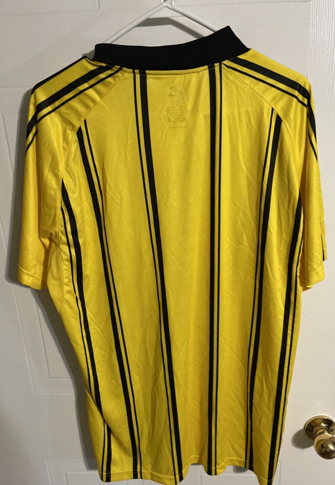 Yellow striped polo new with tags hanging on white hanger against white door background